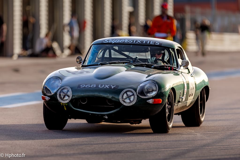 La Jaguar Type E brillant dans la pit lane lors de la course emblématique des 300 km de Dijon, dans la catégorie Super Sixties, à la Dijon Motors Cup 2023, une référence du sport automobile.
